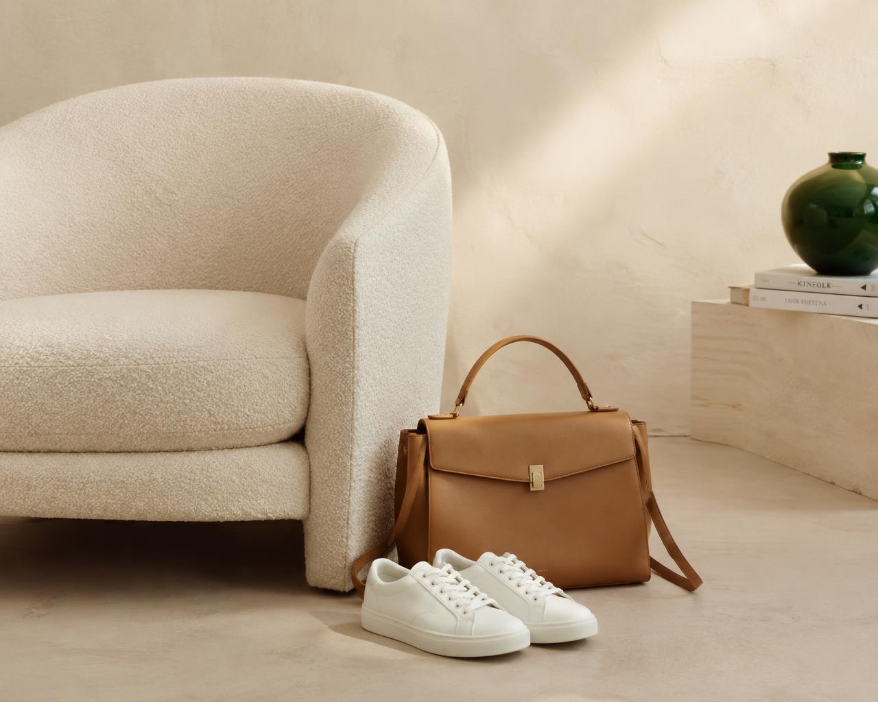 Cream boucle armchair, tan leather handbag and white sneakers in soft light